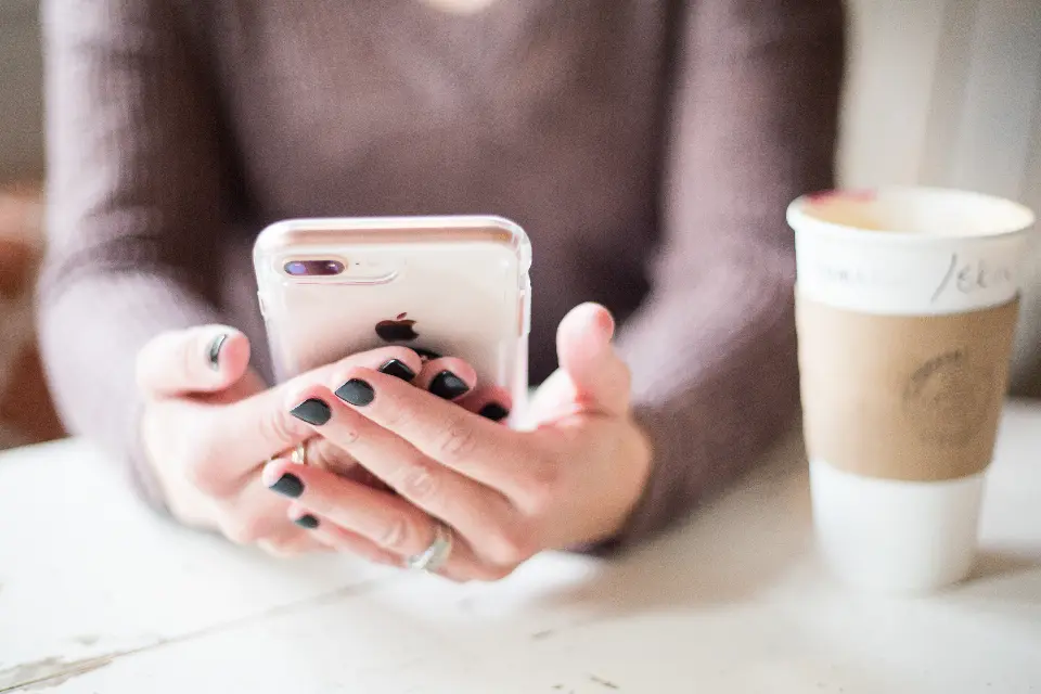 Mani che tengono uno smartphone accanto a una tazza di caffè